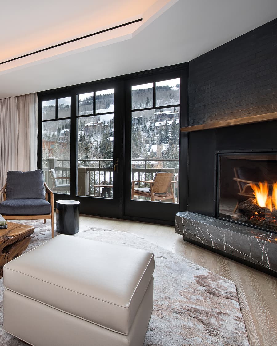 Living room of a residence at Four Seasons Resort and Residences Vail — a lit fireplace, floor-to-ceiling windows, and snow-covered Vail beyond the balcony.